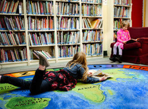 Girl lays on floor while another girl reads