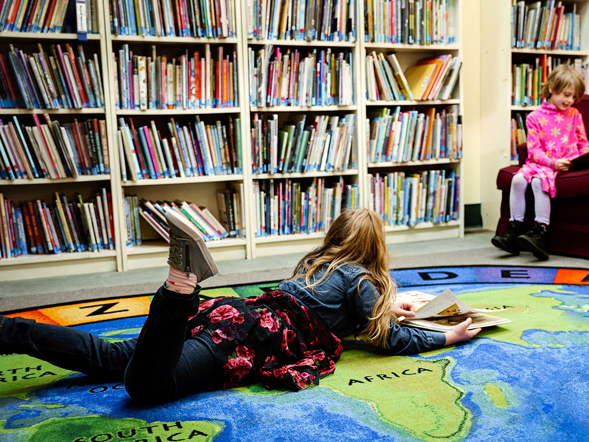 Girl with Blond Hair laying on mat of world in front of library