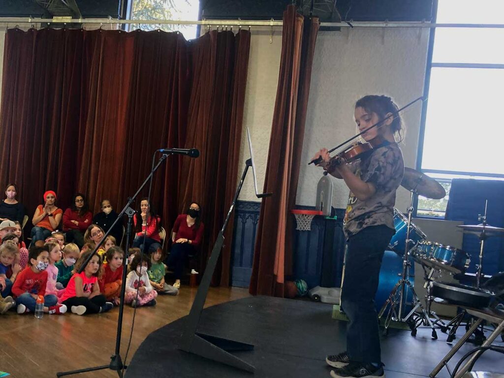 Student holding Violin performs on stage in front of young audience